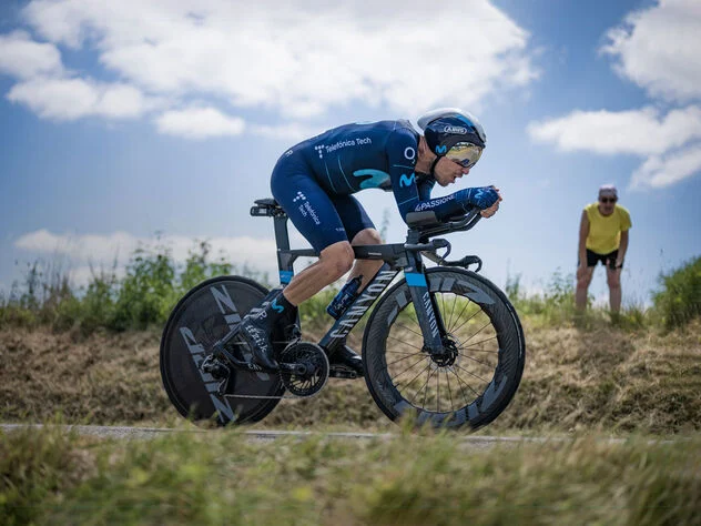 Time trial bike mounted on smart trainer, multiple fans positioned strategically, sweat guard installed, computer mount with power display, professional lighting, clean training space